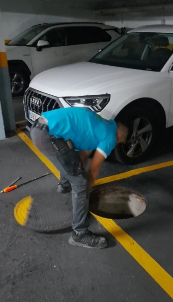 Técnico trabajando en el mantenimiento de una alcantarilla en un estacionamiento-pozarq360